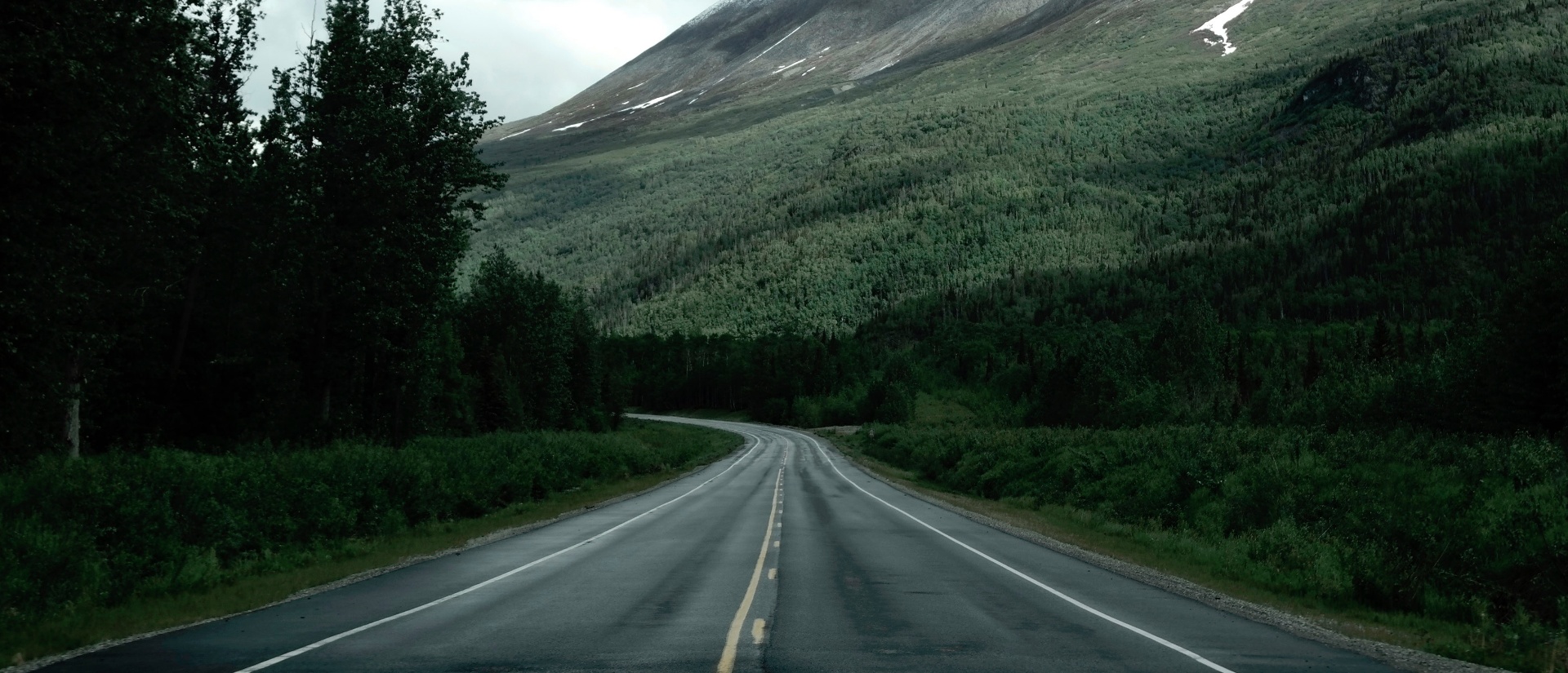 An empty road winding through a forested mountain valley in Canada
